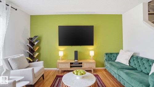 Living area featuring wood-finish flooring, a vibrant accent wall, and recessed staircase - 80 287 Macewan Road, Edmonton, AB - Indoor Photo Showing Living Room