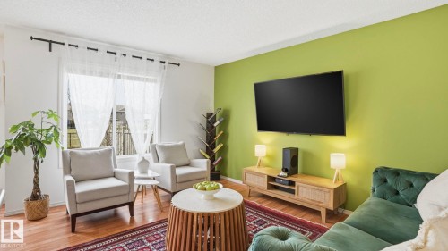 Living space featuring wood-finish flooring and a large window with sheer curtains - 80 287 Macewan Road, Edmonton, AB - Indoor Photo Showing Living Room