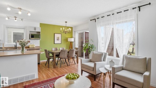 Open-concept living space featuring wood-finish flooring, a kitchen island with seating, white shaker cabinetry, and a dining area with a chandelier - 80 287 Macewan Road, Edmonton, AB - Indoor
