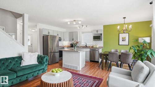 Open-concept living space featuring wood-finish flooring, a kitchen island with seating, stainless steel appliances, a tile backsplash, and overhead track lighting - 80 287 Macewan Road, Edmonton, AB - Indoor