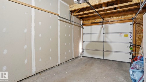 Spacious garage featuring a concrete floor, exposed ceiling joists, and a white panel garage door with an automatic opener - 80 287 Macewan Road, Edmonton, AB - Indoor Photo Showing Garage