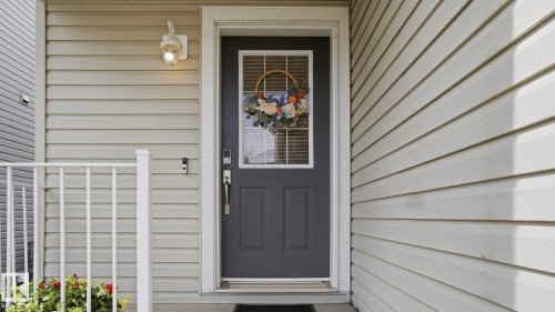 Entryway featuring a dark gray door with an upper window, white trim, and a contemporary wall light fixture - 80 287 Macewan Road, Edmonton, AB - Outdoor With Exterior