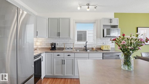 Kitchen featuring light gray cabinetry, stainless steel appliances, a subway tile backsplash, and wood-finish flooring - 80 287 Macewan Road, Edmonton, AB - Indoor Photo Showing Kitchen With Double Sink