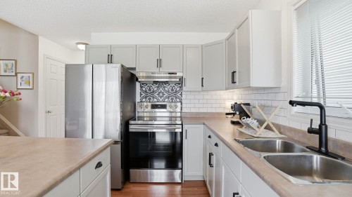 Contemporary kitchen featuring light gray cabinetry with black hardware, stainless steel appliances, a subway tile backsplash, and a patterned accent tile above the range - 80 287 Macewan Road, Edmonton, AB - Indoor Photo Showing Kitchen With Double Sink