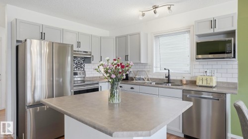 Kitchen featuring light gray cabinetry, stainless steel appliances, a white subway tile backsplash, and a central island with a light-colored countertop - 80 287 Macewan Road, Edmonton, AB - Indoor Photo Showing Kitchen With Double Sink With Upgraded Kitchen