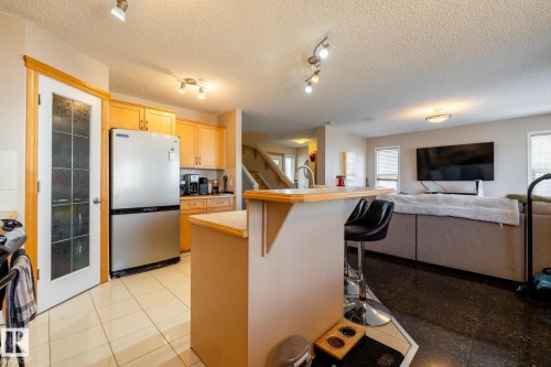 Kitchen featuring wood-finish cabinetry, stainless steel refrigerator, and light-toned countertops - 55 Lamplight Cove, Spruce Grove, AB - Indoor Photo Showing Kitchen
