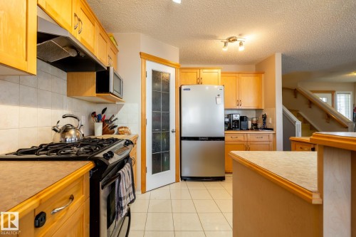 Kitchen featuring wood cabinetry, white tile backsplash, and a black gas range with an overhead range hood - 55 Lamplight Cove, Spruce Grove, AB - Indoor Photo Showing Kitchen