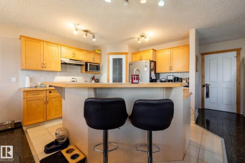 Kitchen featuring wood cabinetry, stainless steel appliances, a breakfast bar, recessed lighting, and tile flooring - 55 Lamplight Cove, Spruce Grove, AB - Indoor Photo Showing Kitchen
