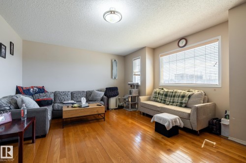 Spacious living area featuring polished wood-finish flooring, neutral wall tones, and multiple windows with horizontal blinds - 55 Lamplight Cove, Spruce Grove, AB - Indoor Photo Showing Living Room