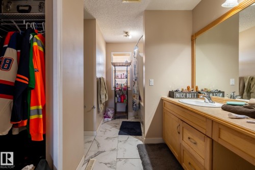 Bathroom featuring a wood-finish vanity with an integrated sink, a large wall-mounted mirror, and tile flooring - 55 Lamplight Cove, Spruce Grove, AB - Indoor Photo Showing Bathroom