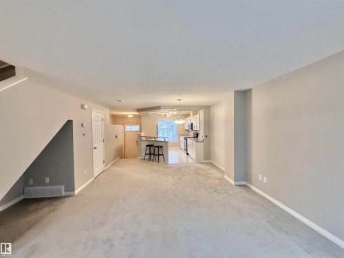Open-concept living area featuring light-colored carpeting, neutral wall tones, and a staircase with wood-finish handrails - 97 465 Hemingway Road, Edmonton, AB - Indoor