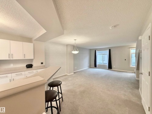Open-concept living area featuring a kitchen bar, light gray carpet, and multiple windows - 97 465 Hemingway Road, Edmonton, AB - Indoor