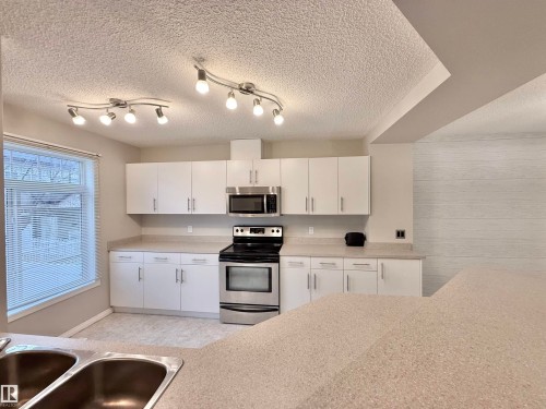 Kitchen featuring white cabinetry, stainless steel appliances, speckled countertops, a double basin sink, and track lighting - 97 465 Hemingway Road, Edmonton, AB - Indoor Photo Showing Kitchen