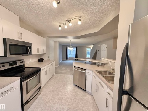 Open-concept kitchen featuring white cabinetry, stainless steel appliances, light-toned countertops, and tile flooring - 97 465 Hemingway Road, Edmonton, AB - Indoor Photo Showing Kitchen With Stainless Steel Kitchen With Double Sink