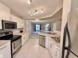 Open-concept kitchen featuring white cabinetry, stainless steel appliances, light-toned countertops, and tile flooring - 