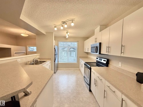 Kitchen featuring light-toned countertops, white cabinetry with brushed nickel hardware, and a stainless steel appliance suite - 97 465 Hemingway Road, Edmonton, AB - Indoor Photo Showing Kitchen With Stainless Steel Kitchen With Double Sink