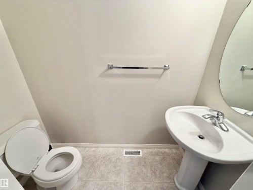 Pedestal sink with chrome faucet, oval wall mirror, and toilet featuring a white seat - 97 465 Hemingway Road, Edmonton, AB - Indoor Photo Showing Bathroom