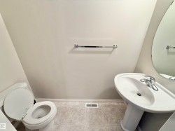Pedestal sink with chrome faucet, oval wall mirror, and toilet featuring a white seat - 