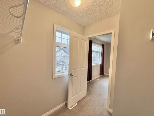 Interior hallway with neutral tone walls and textured ceiling, featuring a wire shelving unit with integrated hanging hooks - 97 465 Hemingway Road, Edmonton, AB - Indoor Photo Showing Other Room