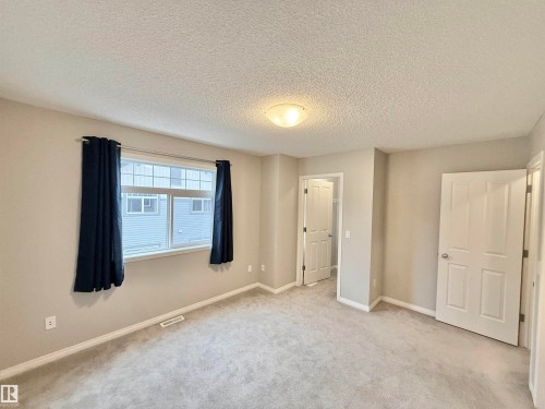 Carpeted room featuring a large window, light-toned walls, white trim, and two paneled doors - 97 465 Hemingway Road, Edmonton, AB - Indoor