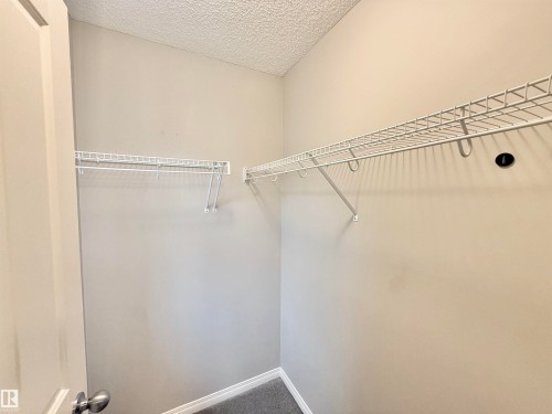 Interior closet space featuring neutral-toned walls, white wire shelving, metal hanging rods, and textured ceiling finish - 97 465 Hemingway Road, Edmonton, AB - Indoor With Storage