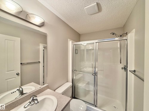 Bathroom featuring a sliding glass shower enclosure with a built-in seat, a light gray speckled countertop with an integrated sink, a chrome faucet, and overhead vanity lighting - 97 465 Hemingway Road, Edmonton, AB - Indoor Photo Showing Bathroom