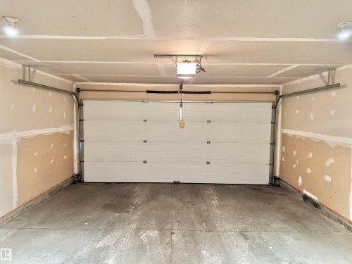 Attached garage featuring a white sectional overhead door with visible track system, concrete flooring, and ceiling-mounted lighting fixtures - 97 465 Hemingway Road, Edmonton, AB - Indoor Photo Showing Garage