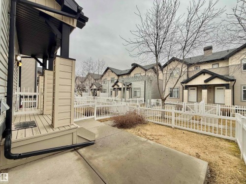 Entry porch with wood-finish decking and white railing, featuring a two-tone exterior with dark trim - 97 465 Hemingway Road, Edmonton, AB - Outdoor
