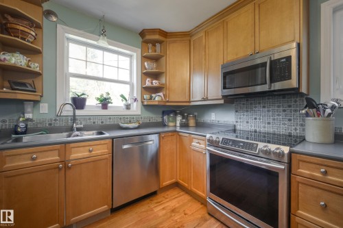 Kitchen featuring warm wood cabinetry, stainless steel appliances, a mosaic tile backsplash, and wood-finish flooring - 11516 72 Avenue, Edmonton, AB - Indoor Photo Showing Kitchen