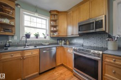 Kitchen featuring warm wood cabinetry, stainless steel appliances, a mosaic tile backsplash, and wood-finish flooring - 