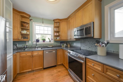 Kitchen featuring light wood-finish cabinetry, stainless steel appliances, dark countertops, and a patterned tile backsplash - 11516 72 Avenue, Edmonton, AB - Indoor Photo Showing Kitchen With Double Sink