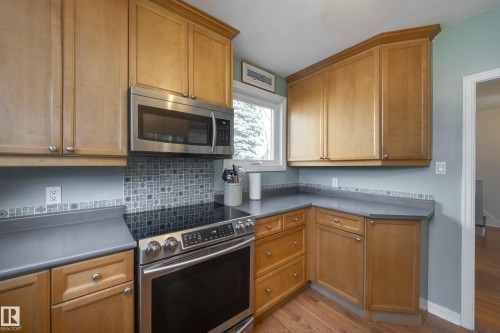 Kitchen featuring light wood cabinetry, a stainless steel over-the-range microwave, a glass-top electric range, a gray countertop, and a decorative tile backsplash - 11516 72 Avenue, Edmonton, AB - Indoor Photo Showing Kitchen