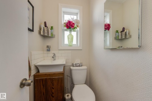 Powder room featuring a pedestal sink with a wood-finish vanity, a window, a toilet, and a wall-mounted mirror - 11516 72 Avenue, Edmonton, AB - Indoor Photo Showing Bathroom