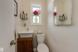 Powder room featuring a pedestal sink with a wood-finish vanity, a window, a toilet, and a wall-mounted mirror - 