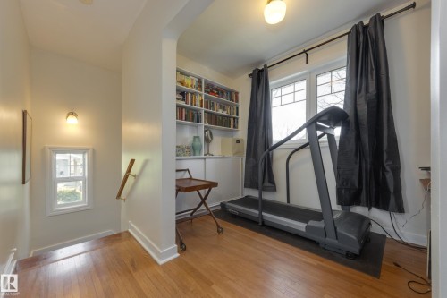Hardwood flooring throughout featuring a built-in shelving unit, a large multi-pane window with dark drapery, and a wall-mounted light fixture - 11516 72 Avenue, Edmonton, AB - Indoor Photo Showing Other Room
