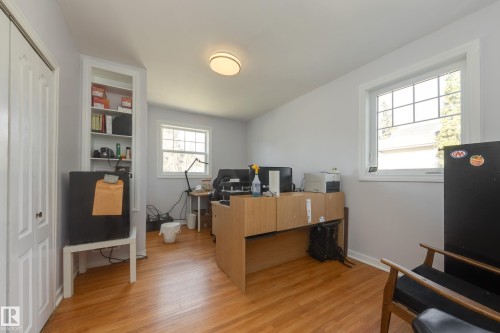 Light-filled interior space featuring two windows with white grilles, wood-finish flooring, a white bi-fold door, and an integrated white built-in shelving unit - 11516 72 Avenue, Edmonton, AB - Indoor Photo Showing Office