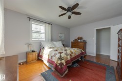 Bedroom featuring wood-finish flooring, light grey painted walls, a window with white trim, and a ceiling fan with integrated lighting - 
