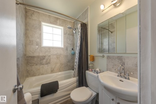 Bathroom featuring a tiled shower surround, built-in bathtub, window with grid pattern, wall-mounted vanity sink, and mirrored medicine cabinet - 11516 72 Avenue, Edmonton, AB - Indoor Photo Showing Bathroom