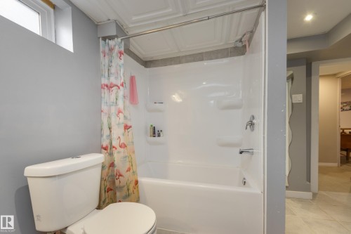 Bathroom featuring a white toilet, a shower-over-tub combination with integrated shelving, and a decorative ceiling panel - 11516 72 Avenue, Edmonton, AB - Indoor Photo Showing Bathroom