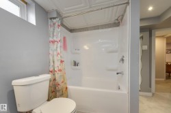 Bathroom featuring a white toilet, a shower-over-tub combination with integrated shelving, and a decorative ceiling panel - 
