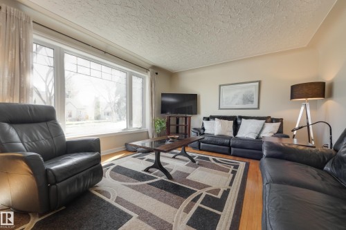 Spacious living area featuring large picture windows, light wood-finish flooring, and a textured ceiling - 11516 72 Avenue, Edmonton, AB - Indoor Photo Showing Living Room