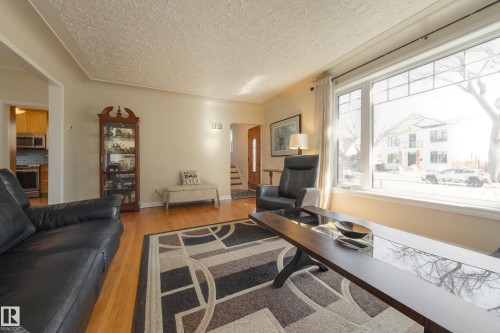 Living area featuring warm-toned wood-finish flooring, a large multi-pane window, and neutral wall tones - 11516 72 Avenue, Edmonton, AB - Indoor Photo Showing Living Room