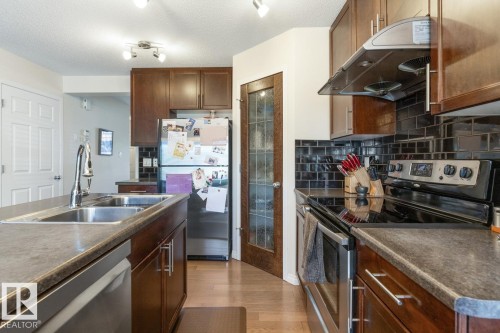 Kitchen featuring dark wood-finish cabinetry, black subway tile backsplash, and stainless steel appliances - 7641 Schmid Crescent, Edmonton, AB - Indoor Photo Showing Kitchen With Stainless Steel Kitchen With Double Sink