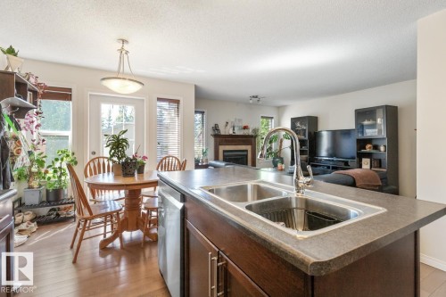 Kitchen island with a double basin stainless steel sink, chrome gooseneck faucet, and dark wood-finish cabinetry - 7641 Schmid Crescent, Edmonton, AB - Indoor Photo Showing Kitchen With Double Sink