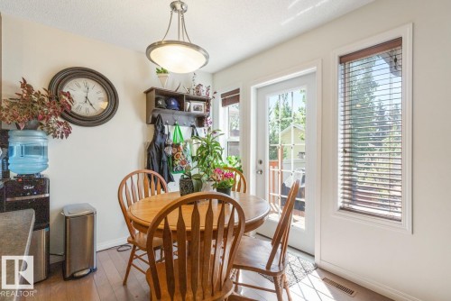 Dining area featuring wood-finish flooring, a white paneled exterior door with glass inserts, an adjacent window with wood blinds, and a contemporary ceiling light fixture - 7641 Schmid Crescent, Edmonton, AB - Indoor Photo Showing Dining Room