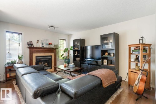 Living area featuring wood-finish flooring, a fireplace with a wood mantle and tile surround, two windows with horizontal blinds, and a built-in ceiling light fixture - 7641 Schmid Crescent, Edmonton, AB - Indoor Photo Showing Living Room With Fireplace