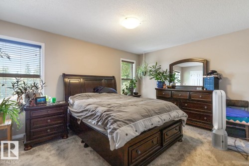 Spacious bedroom featuring neutral wall tones, two windows with blinds, a ceiling-mounted light fixture, and soft carpeting - 7641 Schmid Crescent, Edmonton, AB - Indoor Photo Showing Bedroom