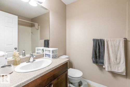 Bathroom featuring a wood-finish vanity with a light-toned countertop, an integrated sink, a chrome faucet, and a wall-mounted mirror - 7641 Schmid Crescent, Edmonton, AB - Indoor Photo Showing Bathroom