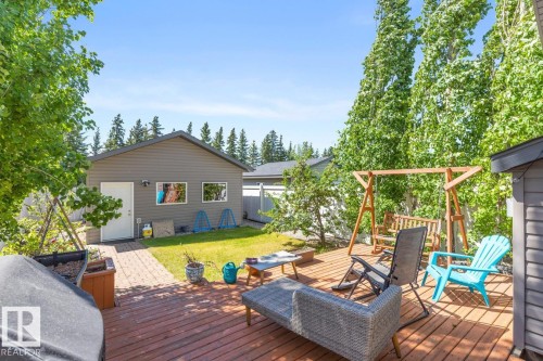 Backyard featuring a spacious wood deck, a manicured lawn, a detached garage with two windows and a side door, a paved walkway, and mature trees - 7641 Schmid Crescent, Edmonton, AB - Outdoor With Deck Patio Veranda With Exterior