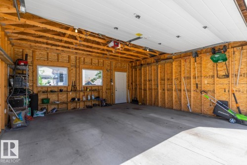 Spacious garage featuring a concrete floor, exposed wood framing, two windows, and a white access door - 7641 Schmid Crescent, Edmonton, AB - Indoor Photo Showing Garage